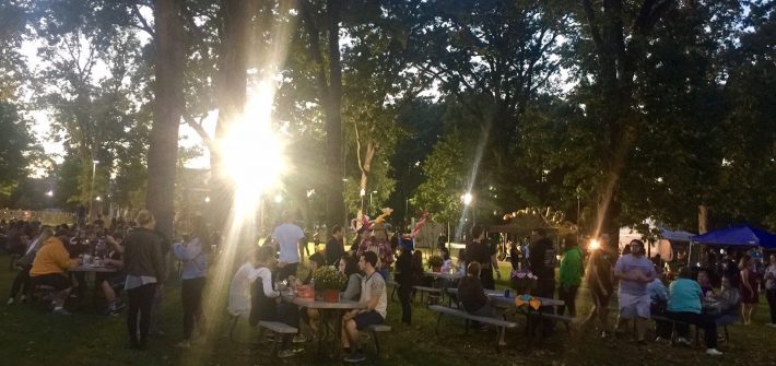 sunlight steams through trees to illuminate students sitting at tables at Homecoming block party