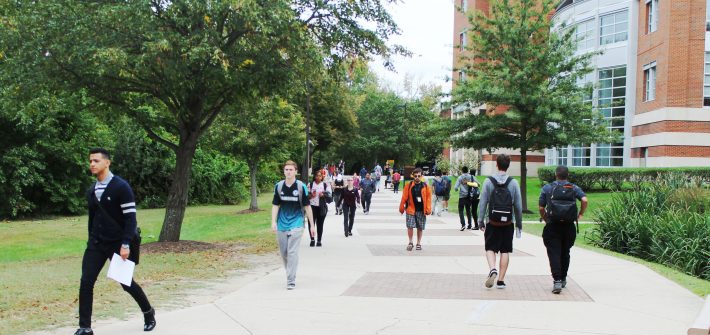 students walk through the middle of campus on a wide sidewalk