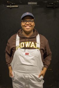 student wears Rowan sweatshirt and gray overalls, smiling at camera
