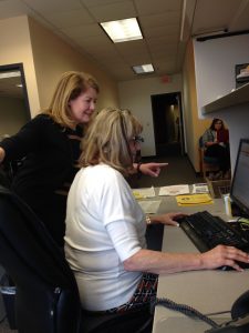 Rory McElwee points at a computer, over someone's shoulder.