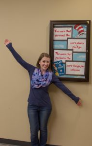 student in front of Dr Seuss reading sign, arms outstretched