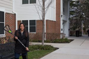 Carly stands outside Rowan Townhouses holding a lacrosse stick