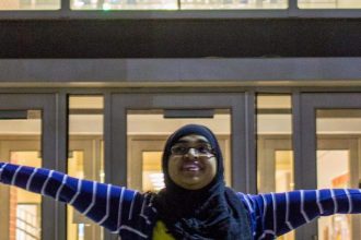 Naveen stands arms outstretched in front of stained glass at James Hall