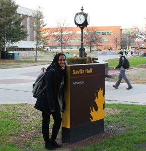 Rowan student Tsion Abay next to the sign of Admissions Building, Savitz Hall