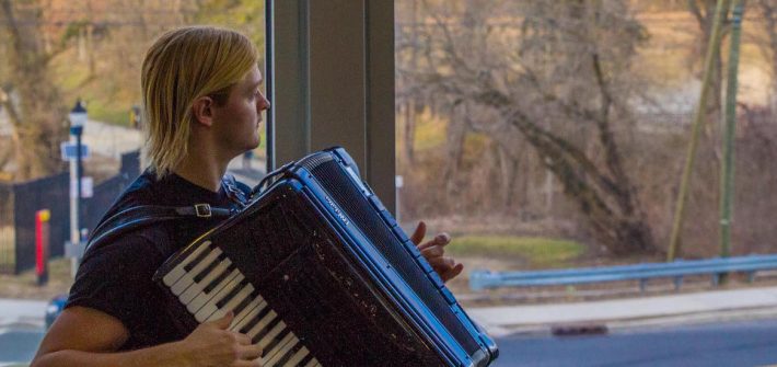 Steve looks out the window at the Glassboro water tower while playing accordian