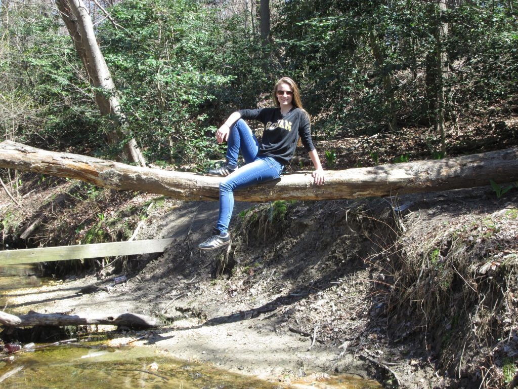 Kelly sits on a fallen tree over a creek