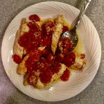 Cooked chicken with chopped grape-tomatoes and garlic in bowl with serving spoon