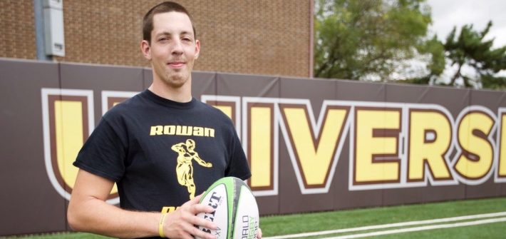 student stands on rowan football field holding a football