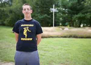 student stands with his arms behind his back, wearing a Rowan rugby tshirt