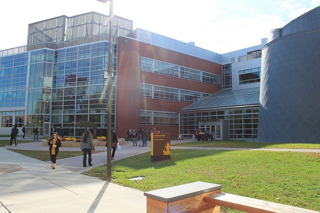 a photo of the front of Science Hall, showing students walking in and out of the building