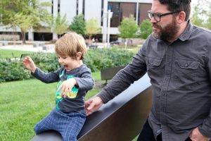 Shane watching is son play outside on statue at Robinson Hall