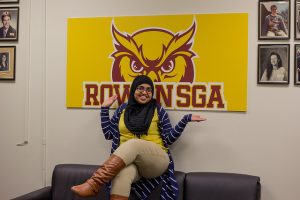 Student Government Association officer sits under an SGA sign with hands upward toward sign