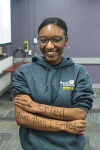 A student stands with her arms crossed, smiling. Her arms read "I cried...but then I smiled."