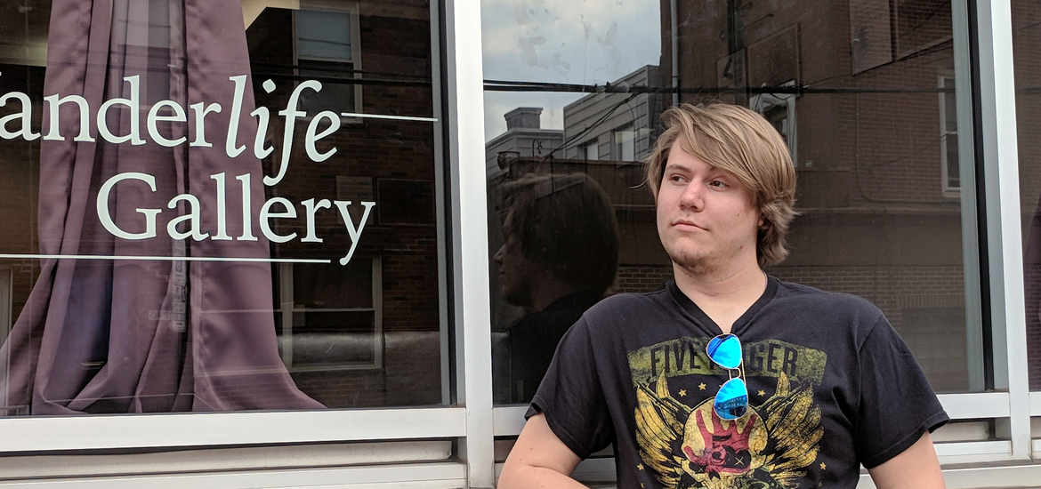 Justin stands next to the glass storefront of Wanderlife Gallery