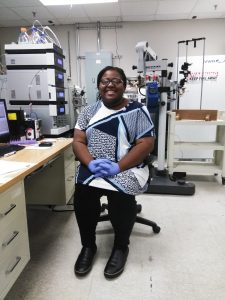 Alana sits in a chair surrounded by lab equipment at her internship