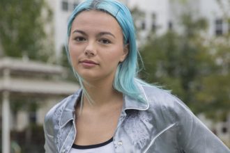 Rowan University student with blue hair wearing a silver silk jacket standing outside Robo