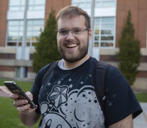 Max, a student wearing a backpack and kirby shirt, plays pokemon go near the library