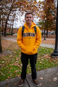 student outside freshmen dorm in rowan hoodie outside of fall trees