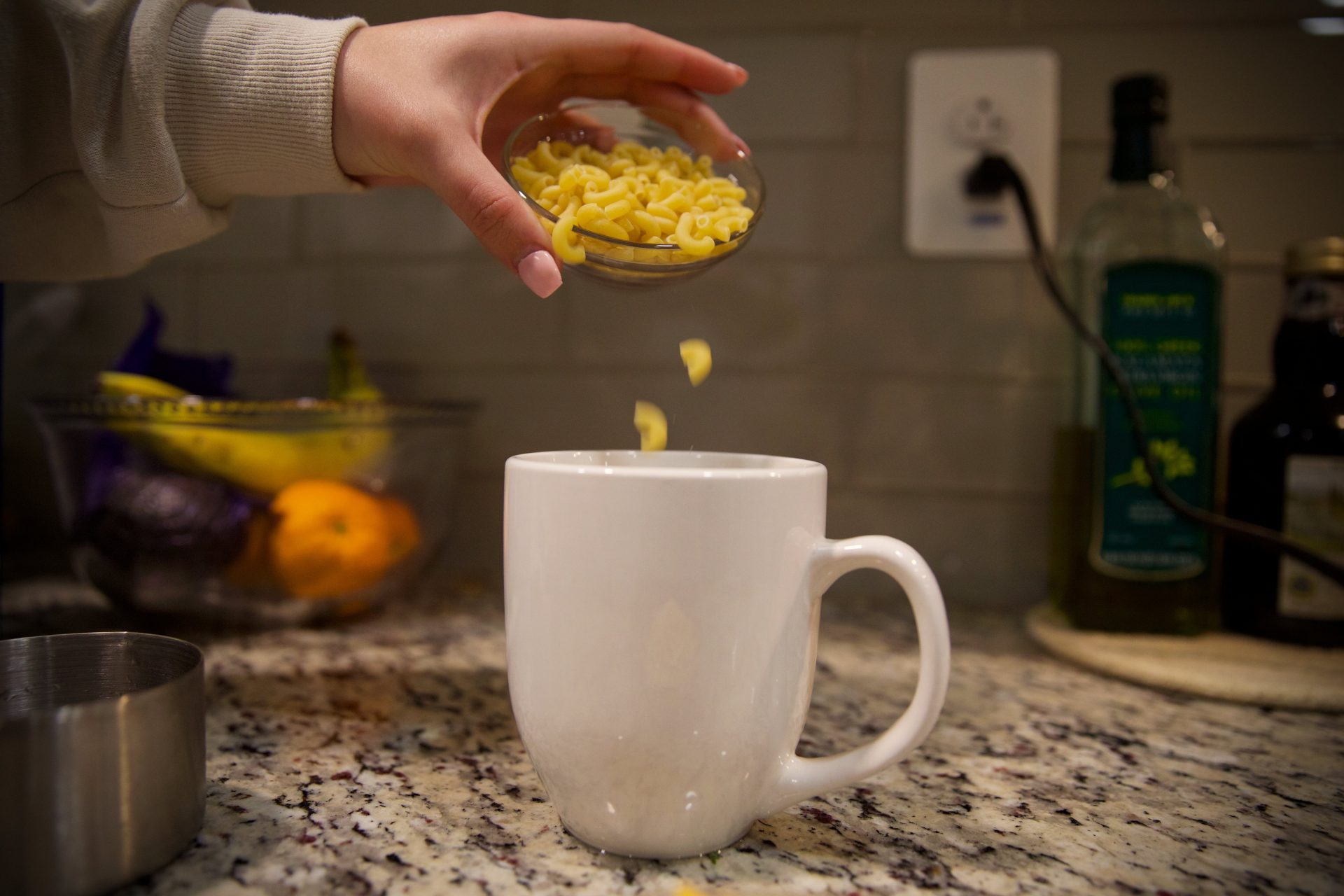 Student pouring macaroni into mug.
