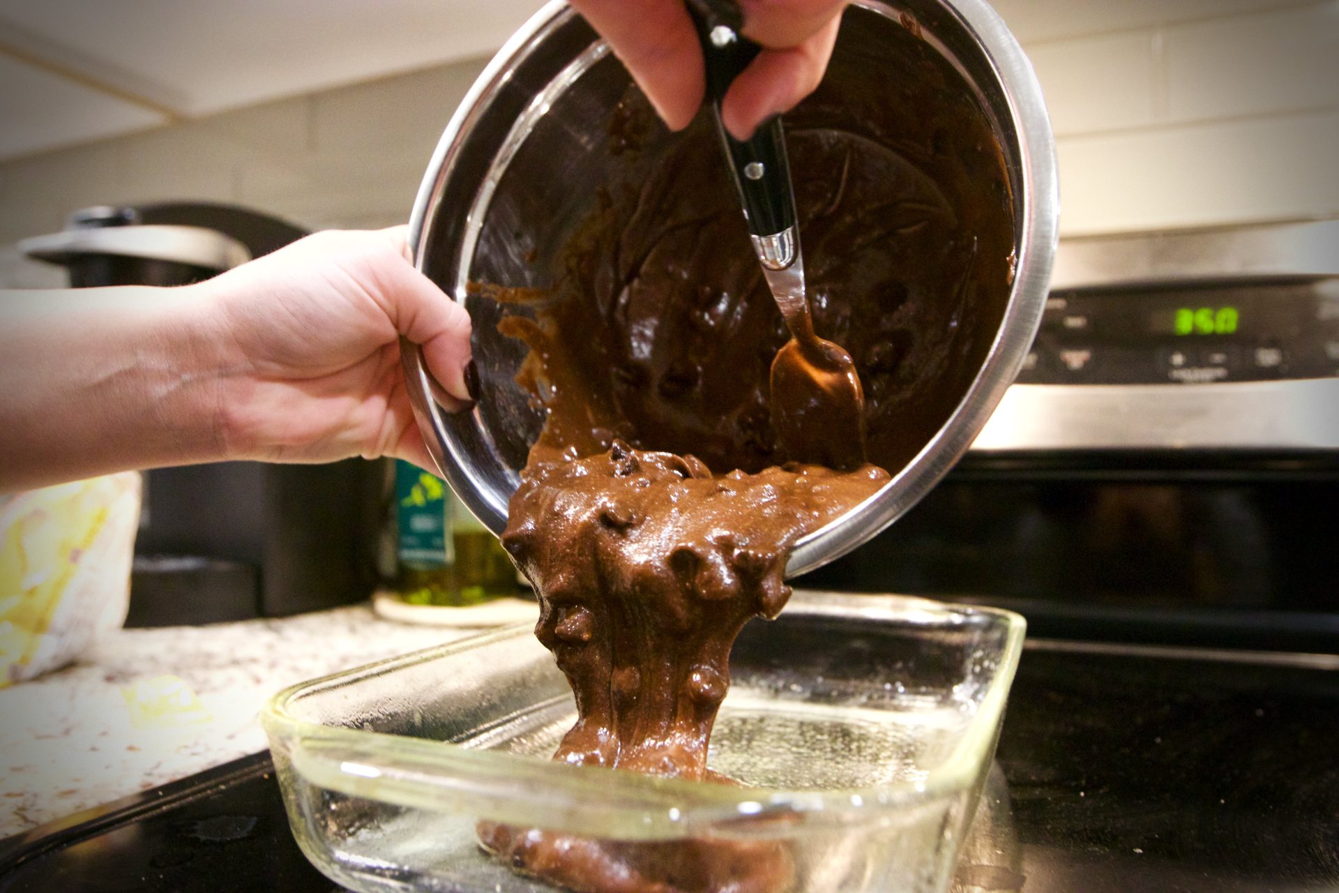Brownie batter being poured into glass pan.
