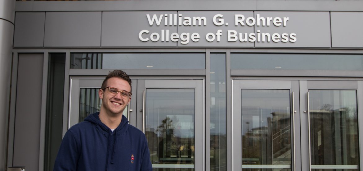 A Rowan student in a blue sweater standing outside the Business Building