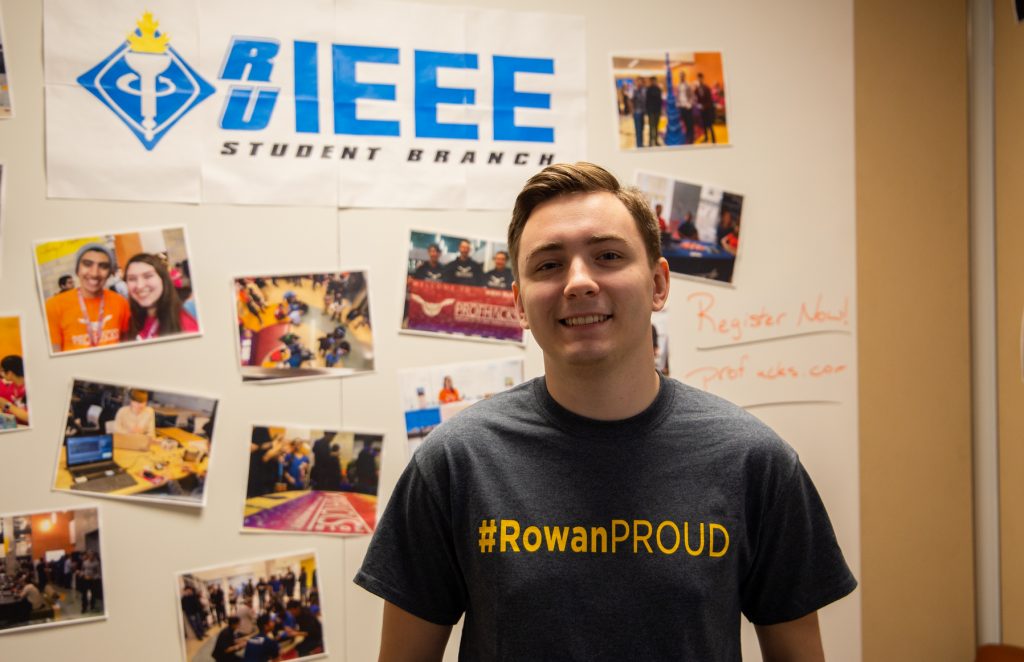 JD stands in front of theh Rowan Engineering IEEE sign wearing a #RowanPROUD t-shirt