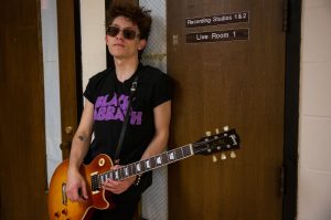 Luke inside Wilson Hall holding guitar in front of Live Recording Studio room