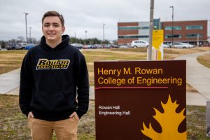 standing in Rowan hoodie next to Henry M. Rowan College of Engineering sign 