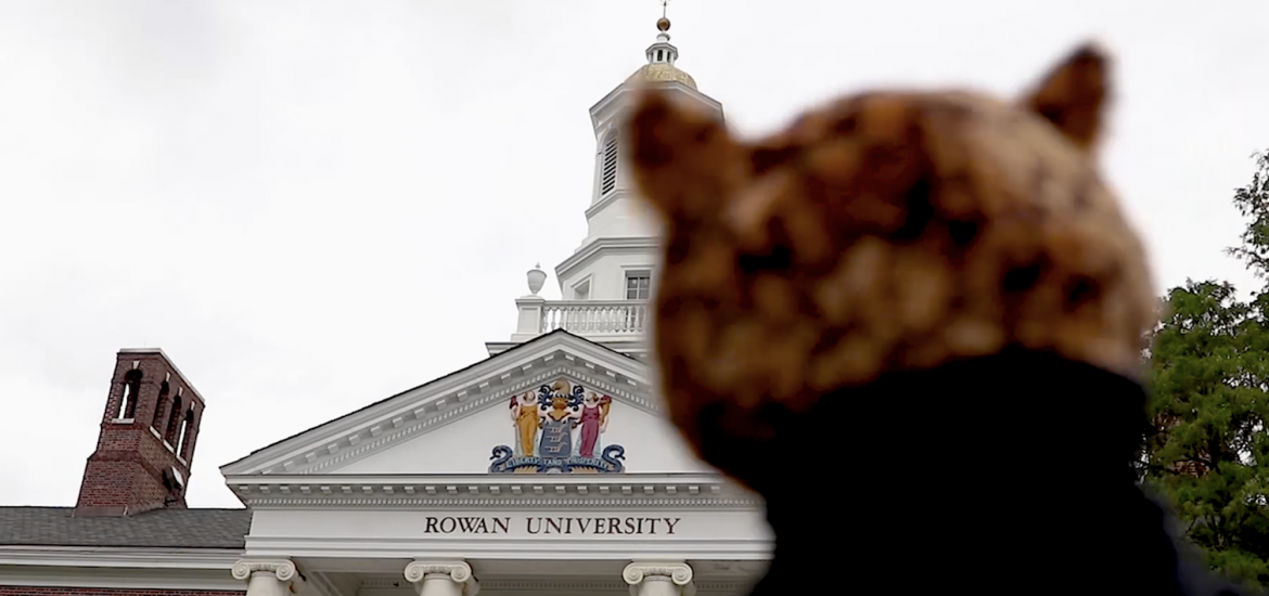 blurred figure in foreground with Rowan University brick and marble building in background