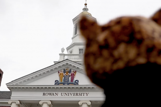 blurred figure in foreground with Rowan University brick and marble building in background