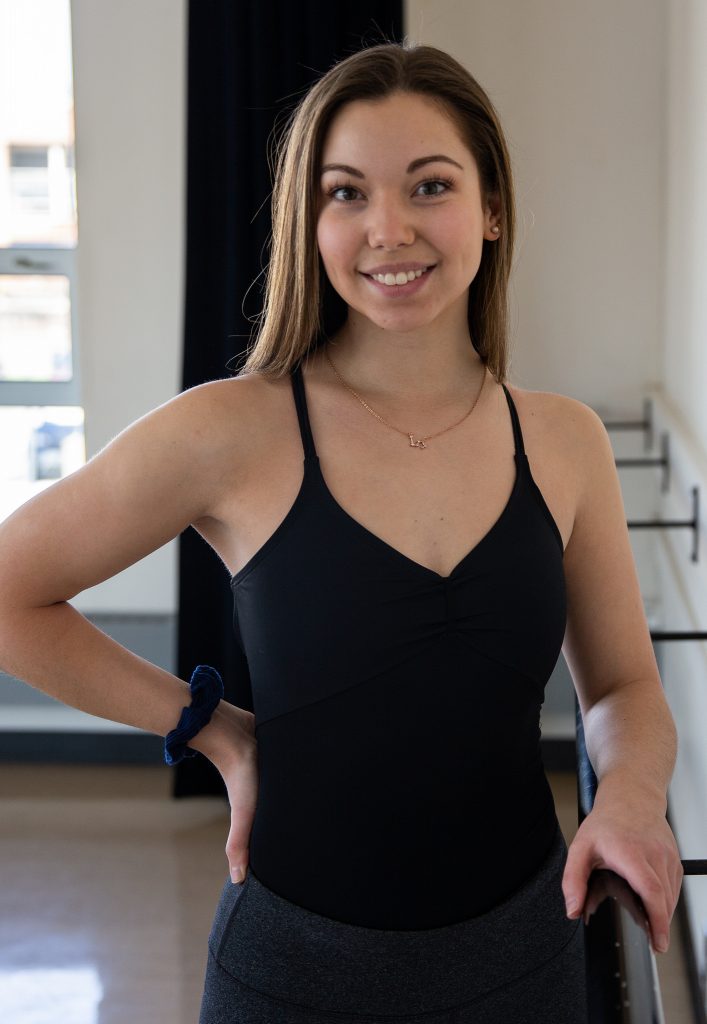 Haley in leotard on the bar in the dance studio facing camera 