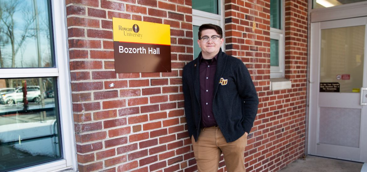 Brandon outside Bozarth Hall in Rowan sweater, in front of brick wall