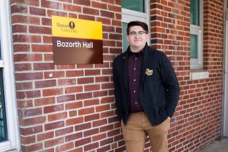 Brandon outside Bozarth Hall in Rowan sweater, in front of brick wall