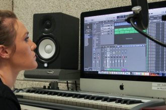 Claire sits at a table with a Mac computer and microphone to work on a song in Wilson Hall's private recording studio.