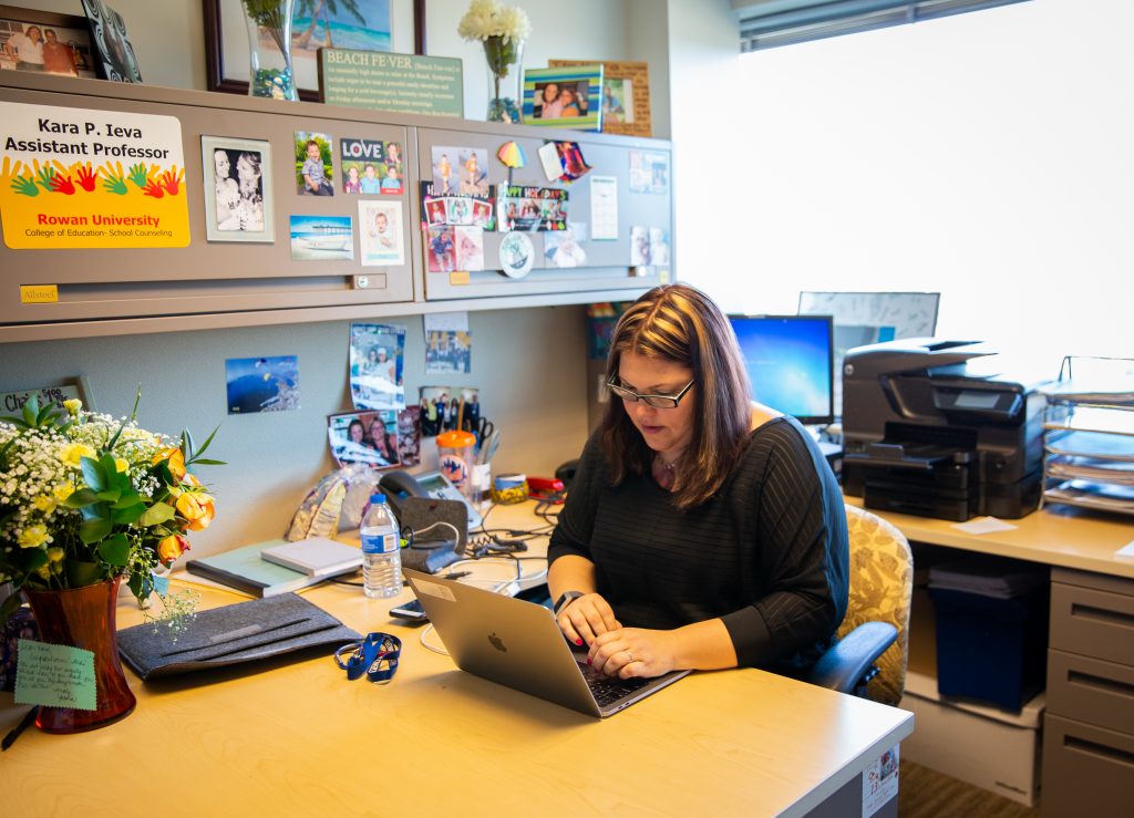 Kara inside her office sitting at her desk with family photos and flowers on the desk
