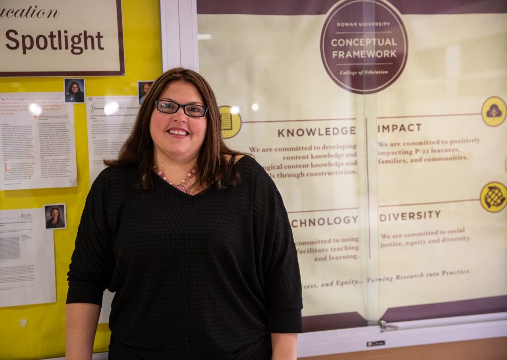 Dr. Ieva standing inside James Hall next to Faculty Spotlight board