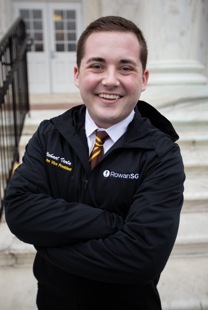 Mike wearing his SGA jacket, the organization he is VP of, standing outside of Bunce steps