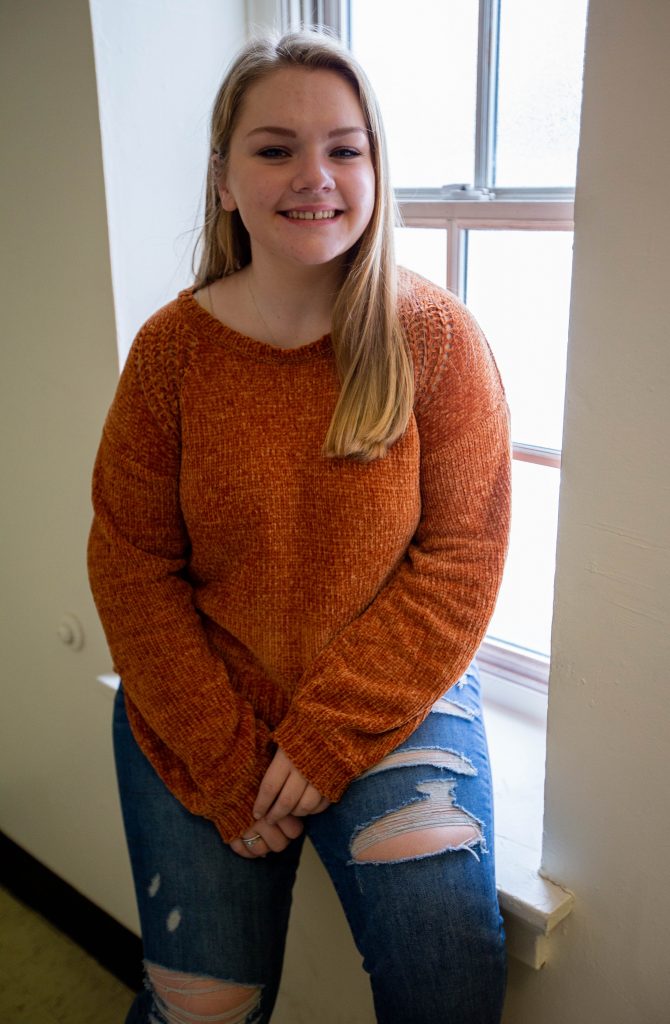 Cassidy smiling in front of a window with orange shirt on