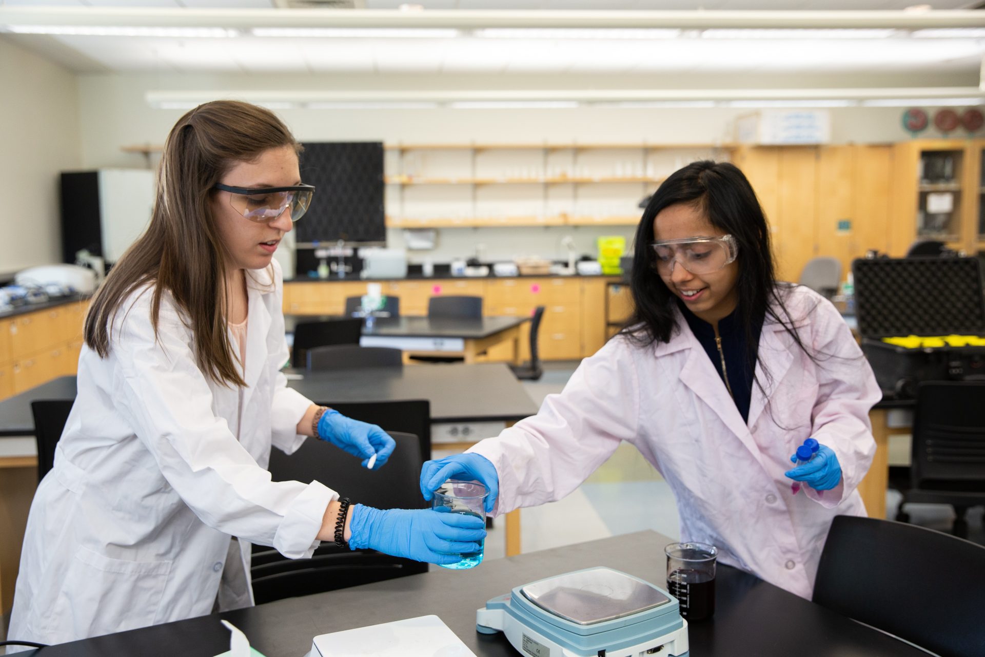 Gatha Adhikari handing a beaker to her professor in Science Hall.