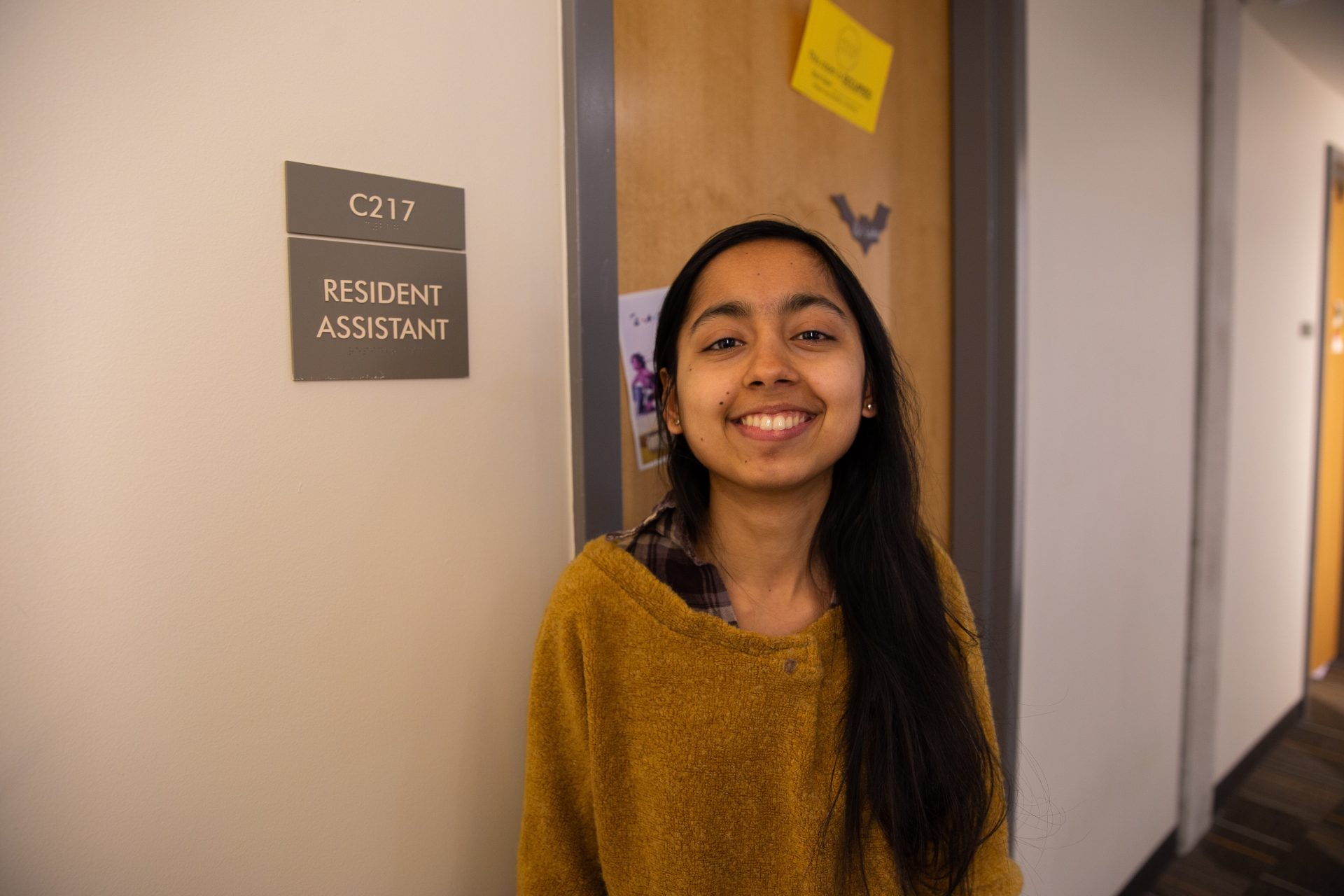 Gatha Adhikari posing in front of her Resident Assistant sign in Holly Pointe Commons.