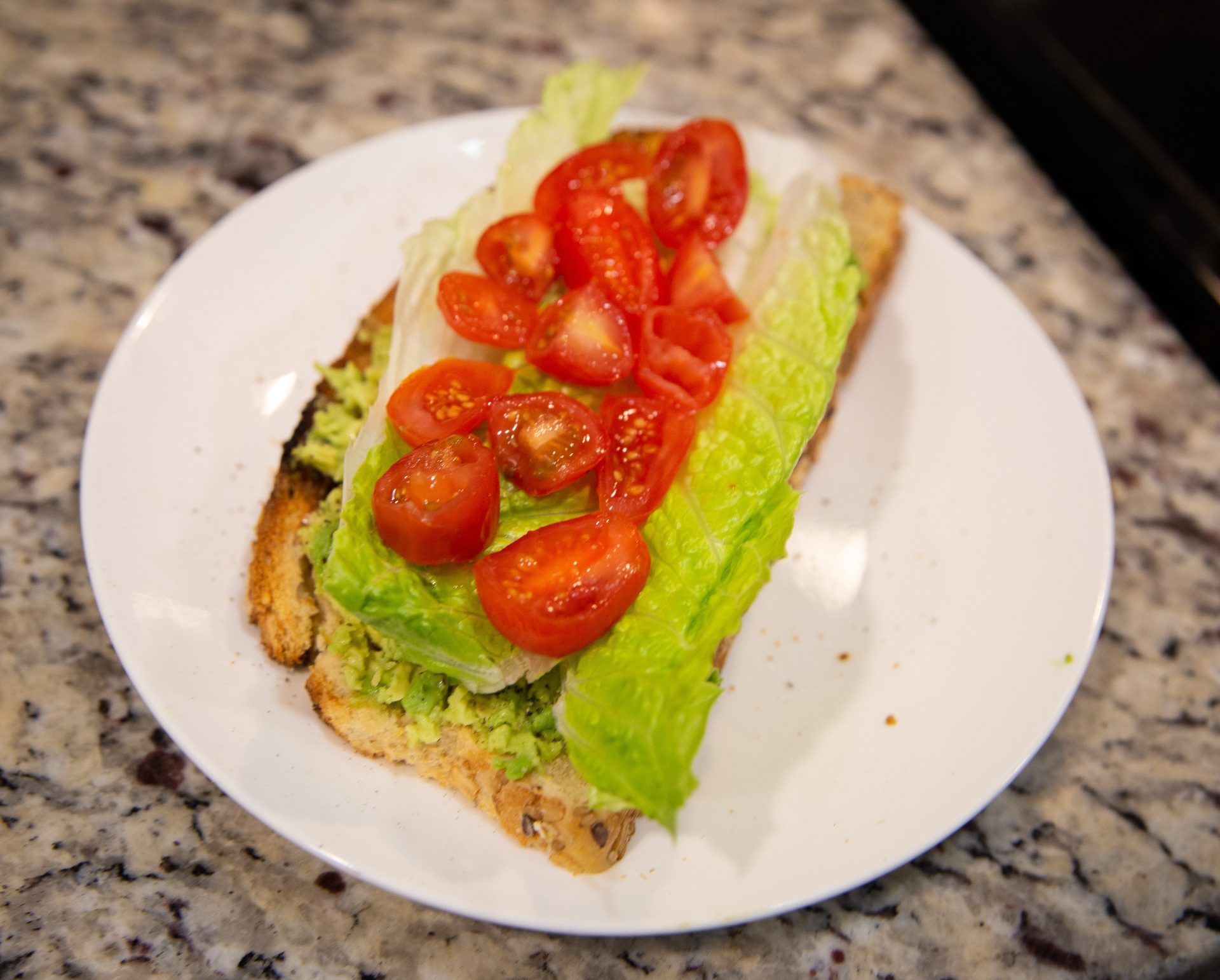Toast topped with avocado, lettuce and tomatoes.