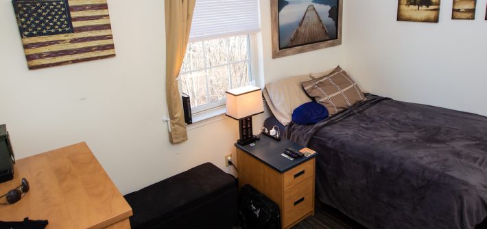 Inside student dorm with one bed, a side table, a dresser, and several pictures on the walls