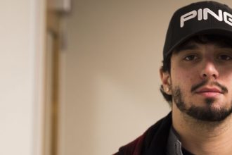 Robert stands in his doorway of Holly Pointe at Rowan University wearing a black jacket and staring at the camera