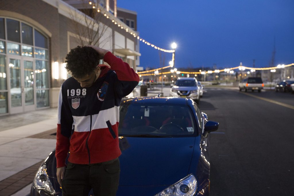 Hashim poses by his car outside on Rowan Blvd at night with his car.