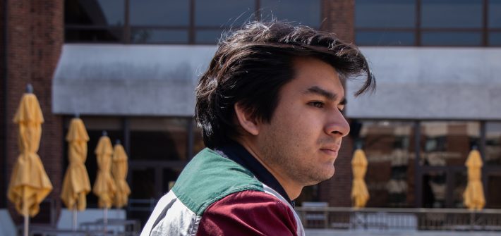 young male student leaning over a railing with a contemplating look on his face