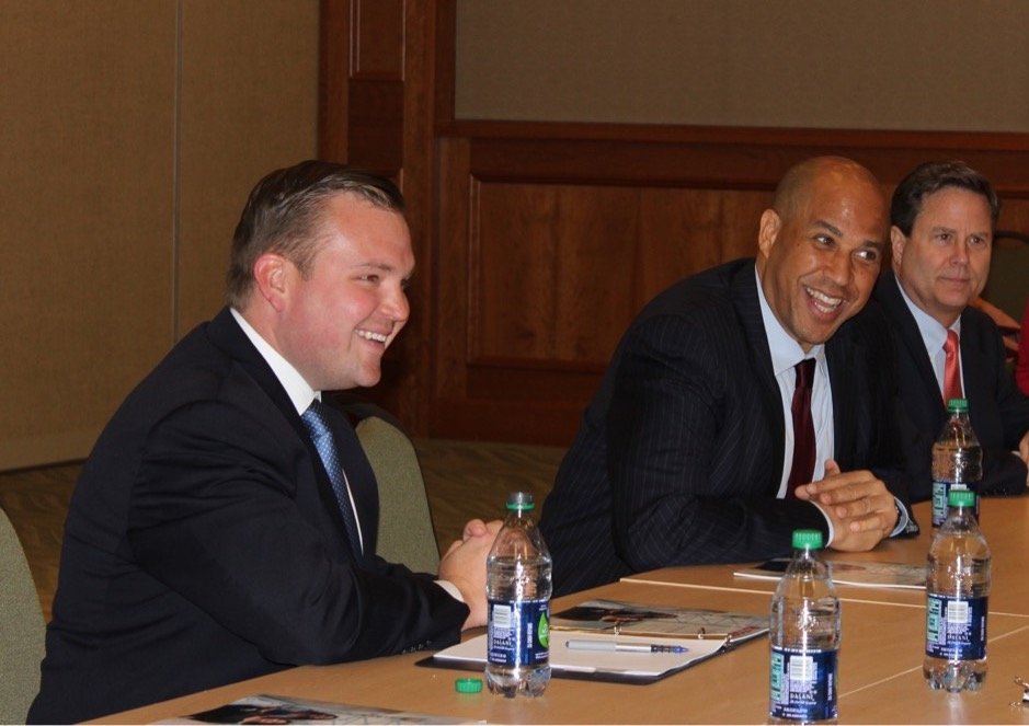 Bill Moen sits at a conference table next to Cory Booker.