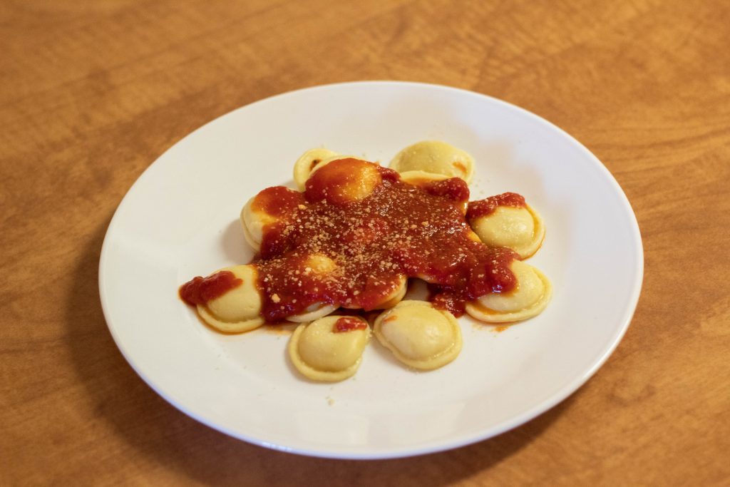 On a plate are small cheese raviolis. They are topped with marinara sauce and parmesan cheese.