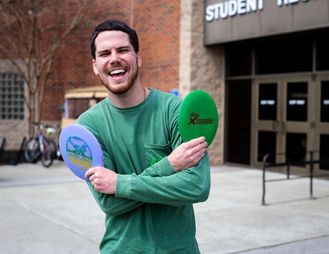 Austin laughs while holding two frisbees outside of Rowan University Rec Center