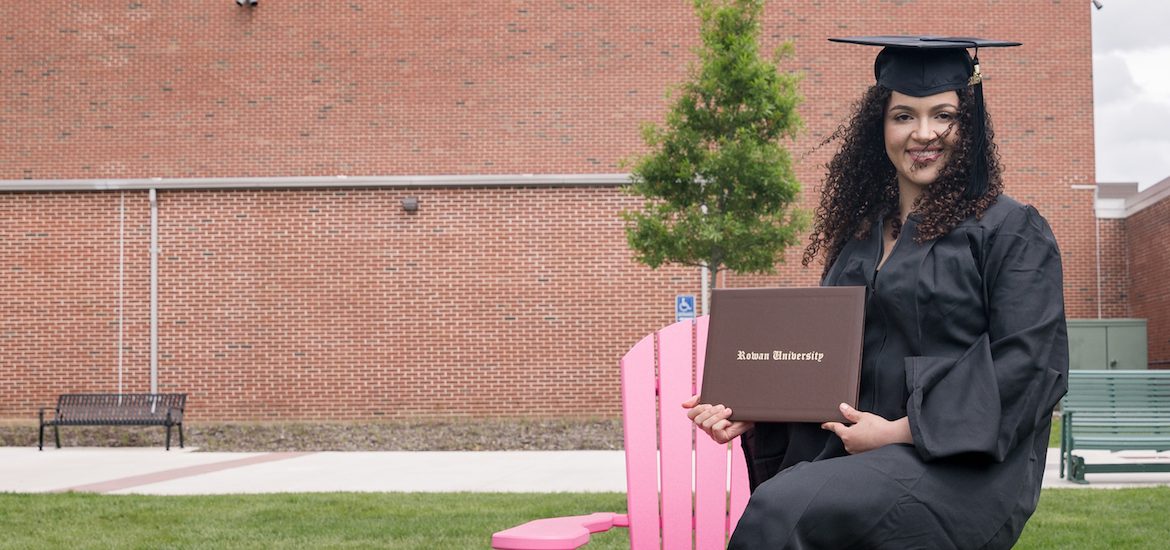 Eduarda in her graduation gown sitting on a pink wooden chair