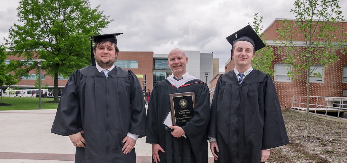 history grads pose with professor, wearing graduation gowns at Rowan University